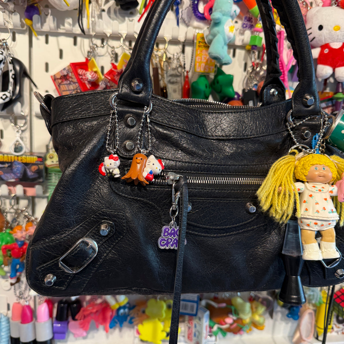 Black handbag with vintage Hello Kitty and Cappage Patch Kids charms in a store setting
