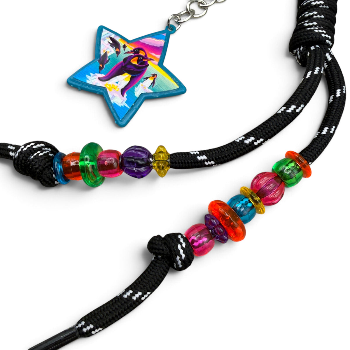 Lisa Frank penguin star keychain beside multicolor beads on black-and-white paracord