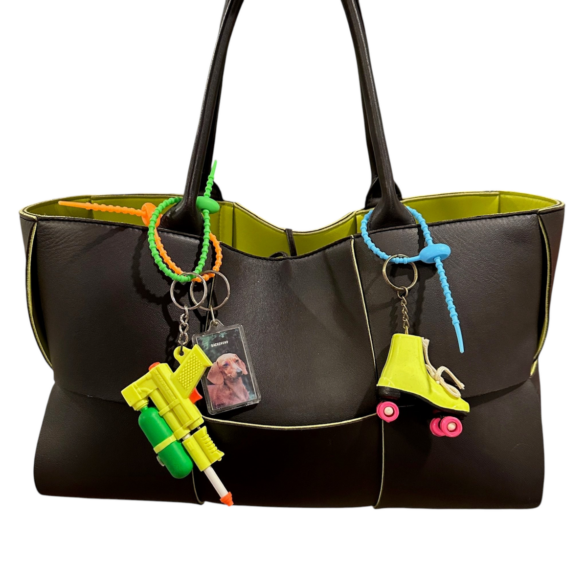 Bag Crap rubber zip tie keychain attachments in primary colors secured on a black tote bag handle with charms