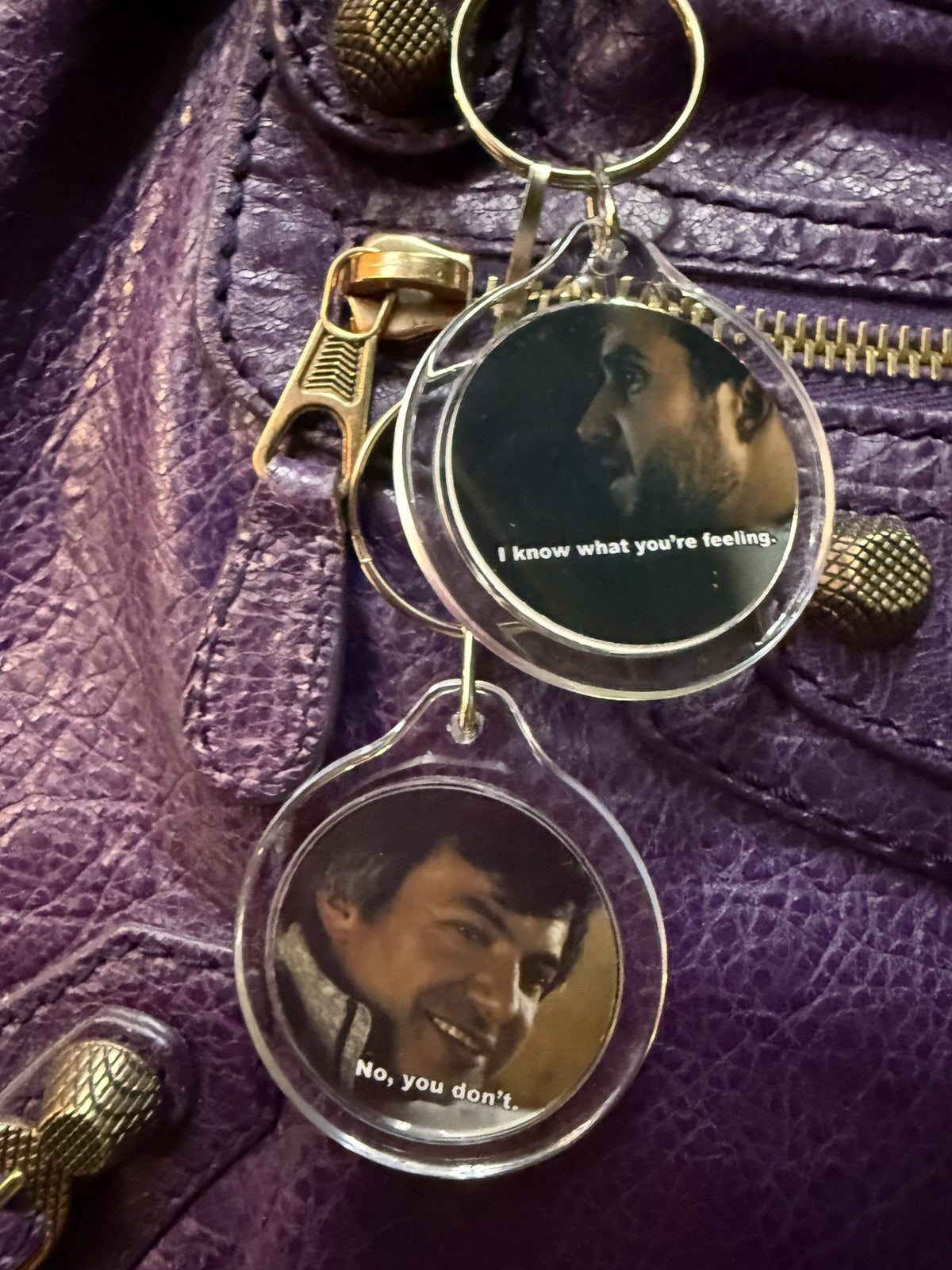 Both sides of the Nathan Fielder meme keychain bag charm styled on a purple leather handbag