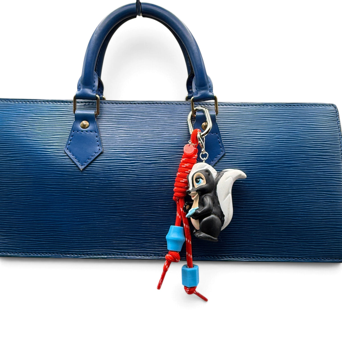 Flower the Skunk red paracord bag charm styled on a blue handbag